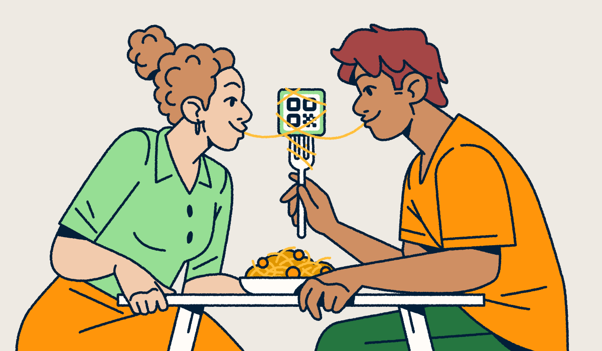 A couple sitting at a table sharing a bowl of spaghetti and meatballs. One partner is holding a fork with a QR Code on it and a piece of spaghetti wrapped around it. They each have one end of the noodle in their mouth.